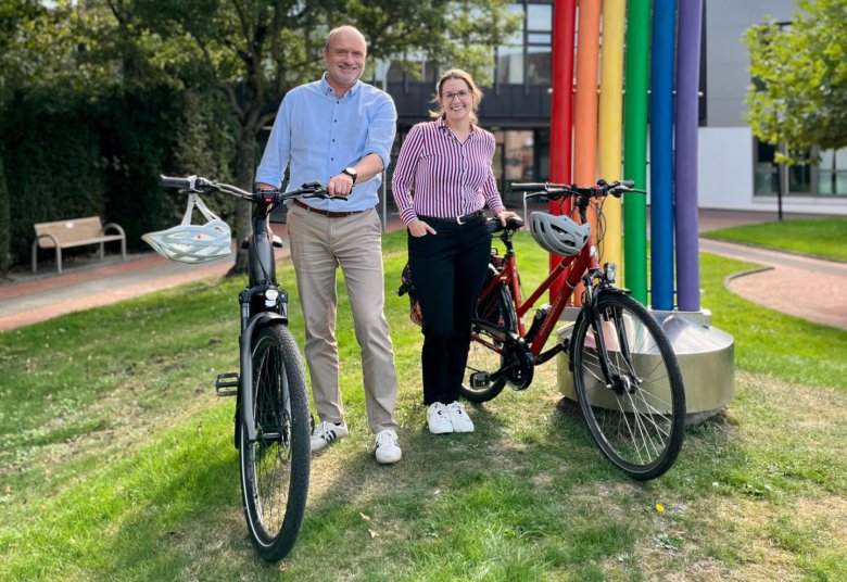 Bürgermeister Klaus Vorderbrüggen steht mit der Klimaschutzbeauftragten Jennifer Vogel mit Fahrrädern vor der Regenbogenskulptur