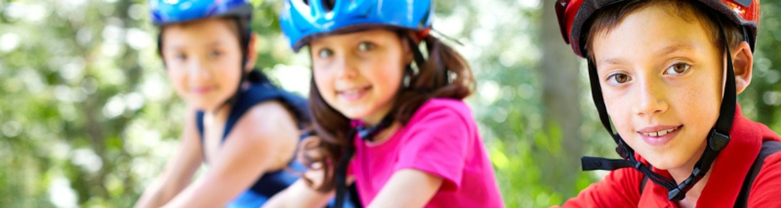 drei Kinder jeweils auf einem Fahrrad. Das Bild hat eine fröhliche Grundstimmung.