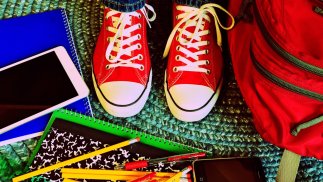 Rote Schuhe im Vordergrund, bunte Schul-Utensilien sind um die Schuhe platziert und zeigen ein fröhliche Grundstimmung.
